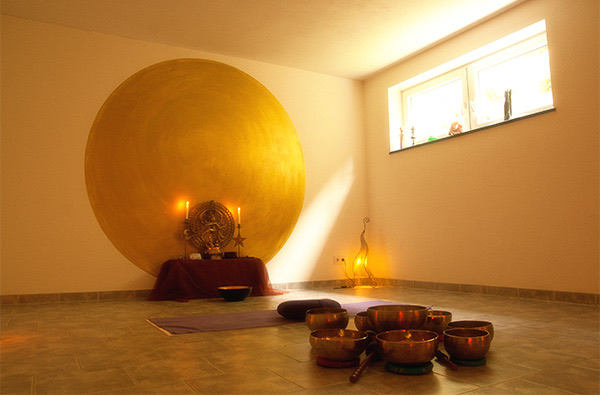Yogaraum mit goldener Scheibe an der Wand, Klangschalen am Boden